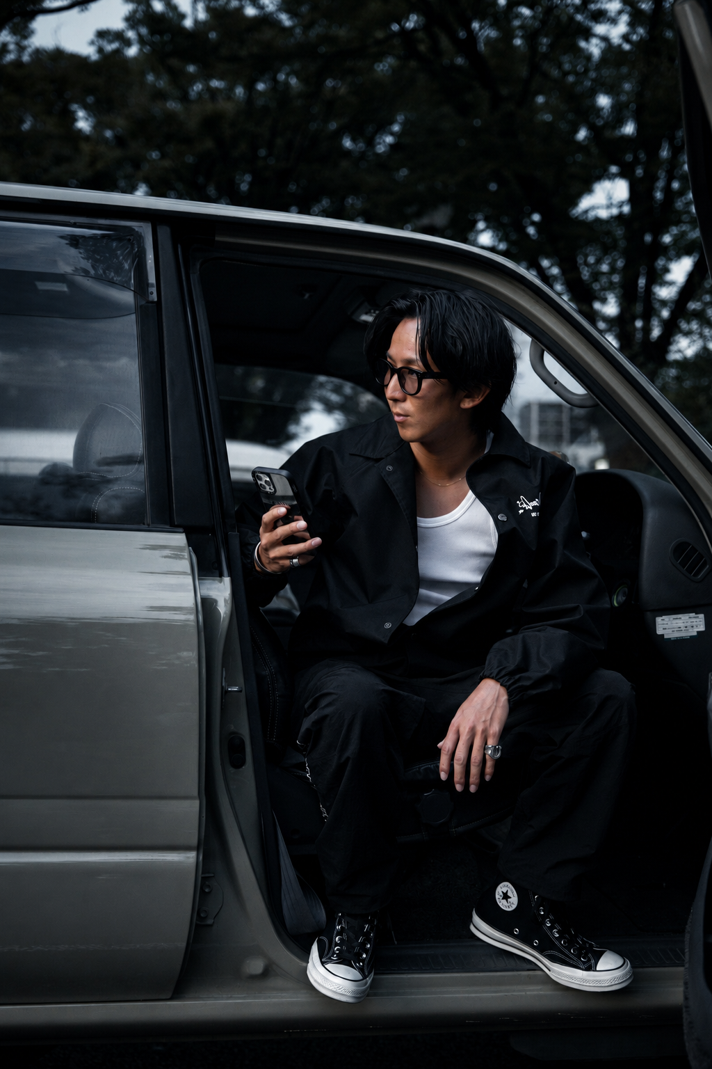 車のドアに腰掛けスマートフォンを持つ男性