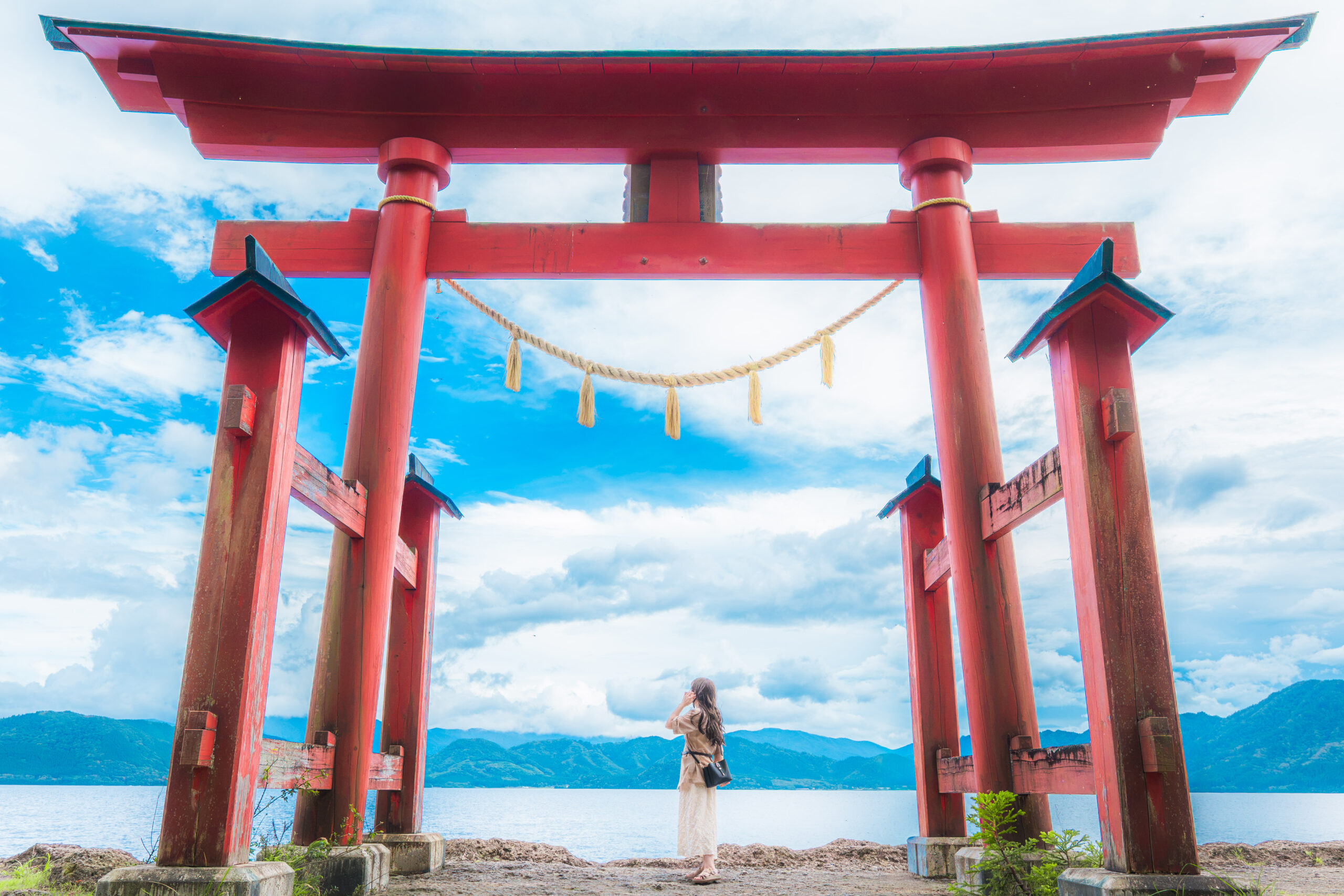 湖畔に立つ大きな赤い鳥居と山並みを背景にした女性のロケーションポートレート