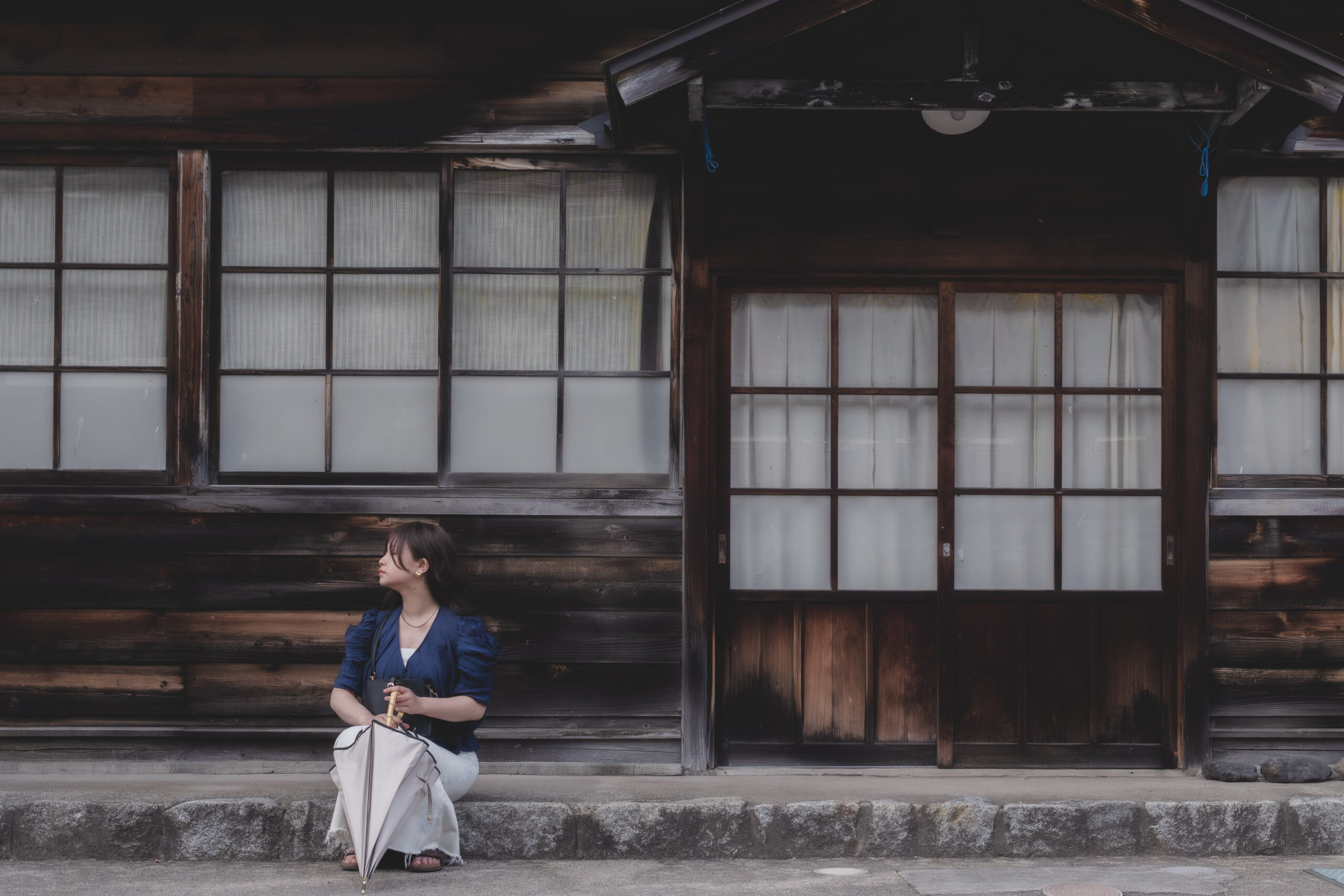 奈良井宿の木造建築前に腰掛けて街を眺める女性の自然なロケーションポートレート