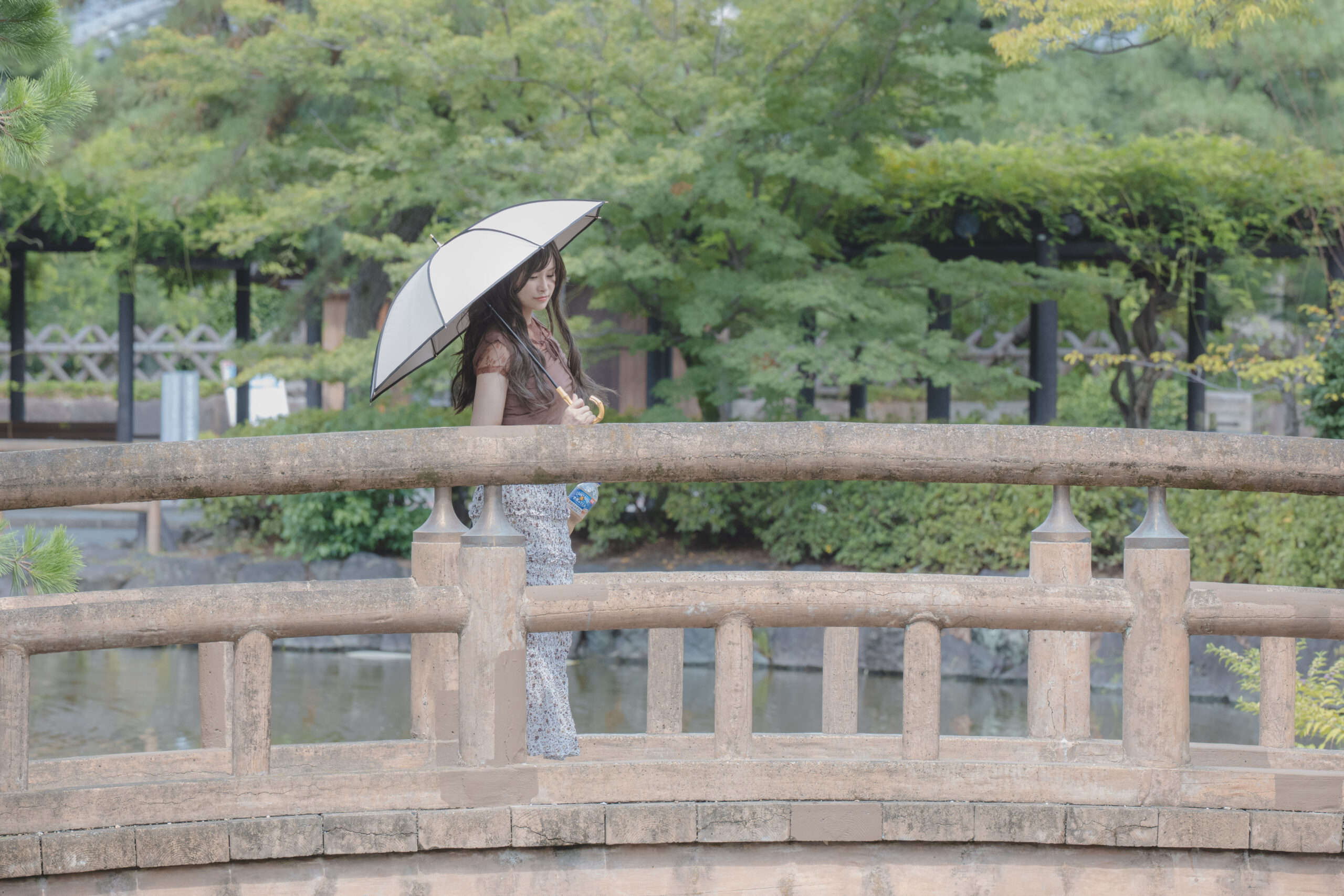 緑に囲まれた橋を日傘を差して歩く女性を自然に撮影した旅先ポートレート